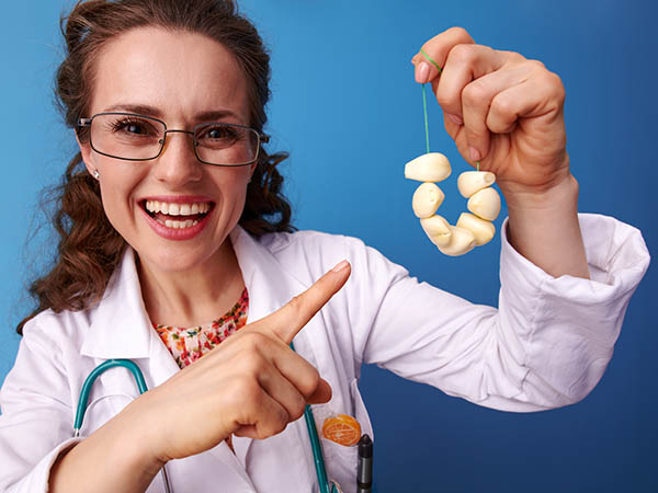 smiling paediatrist woman in white medical robe pointing at garlic beads isolated